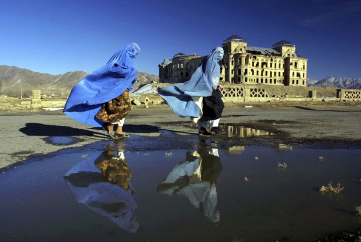 Afghan women in burqas walk in front of the Darulaman Palace in Kabul, Afghanistan on February 3, 2002 on a breezy winter day. The palace lies in ruins, it once was the materpiece of Kabul built by King Amanullah.